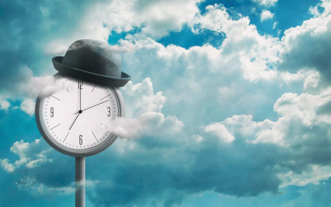 A clock with a hat on surrounded by blue sky and fluffy white clouds.